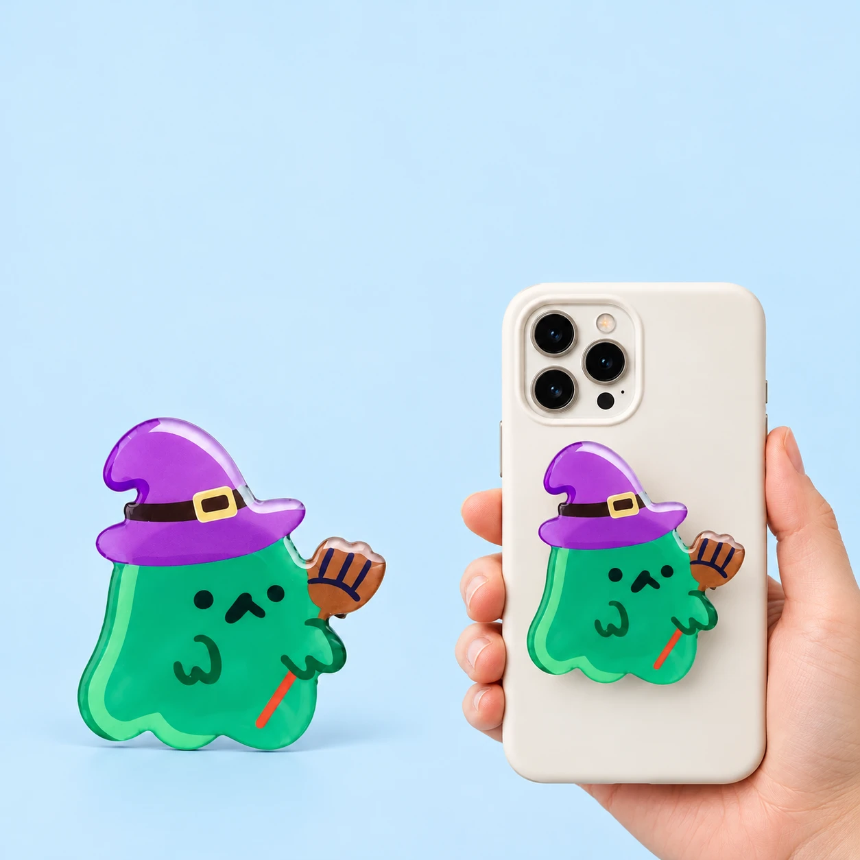 Green ghost expandable phone grip with purple witch hat and broom in closed phone-back placement, square composition
