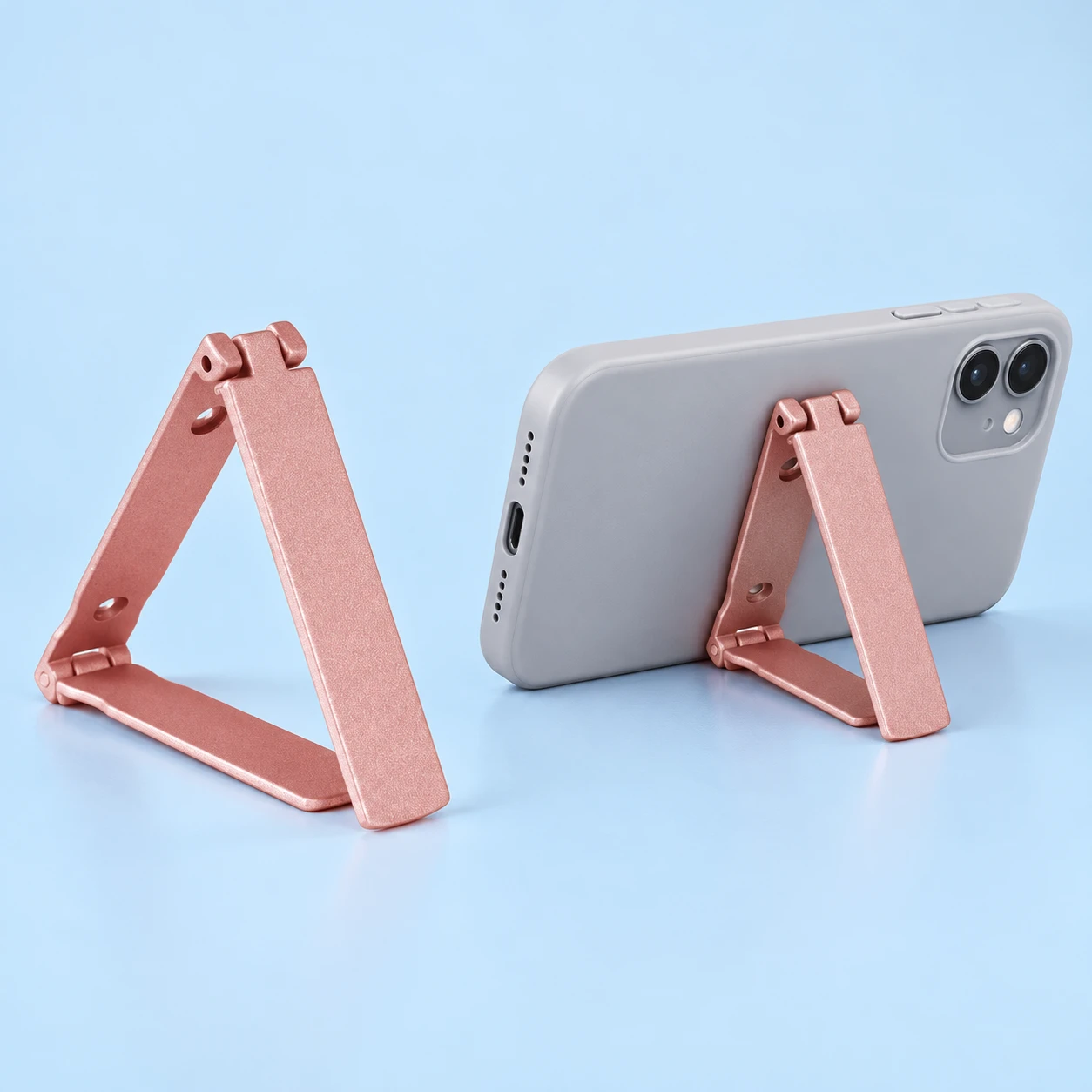 Rose-pink three-panel phone-back kickstand with two hinges, shown complete and supporting a landscape phone; rear attachment method is unspecified.