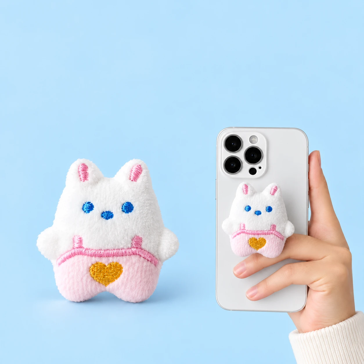 White plush bunny phone grip in pink heart overalls with illustrative closed phone mounting, square composition