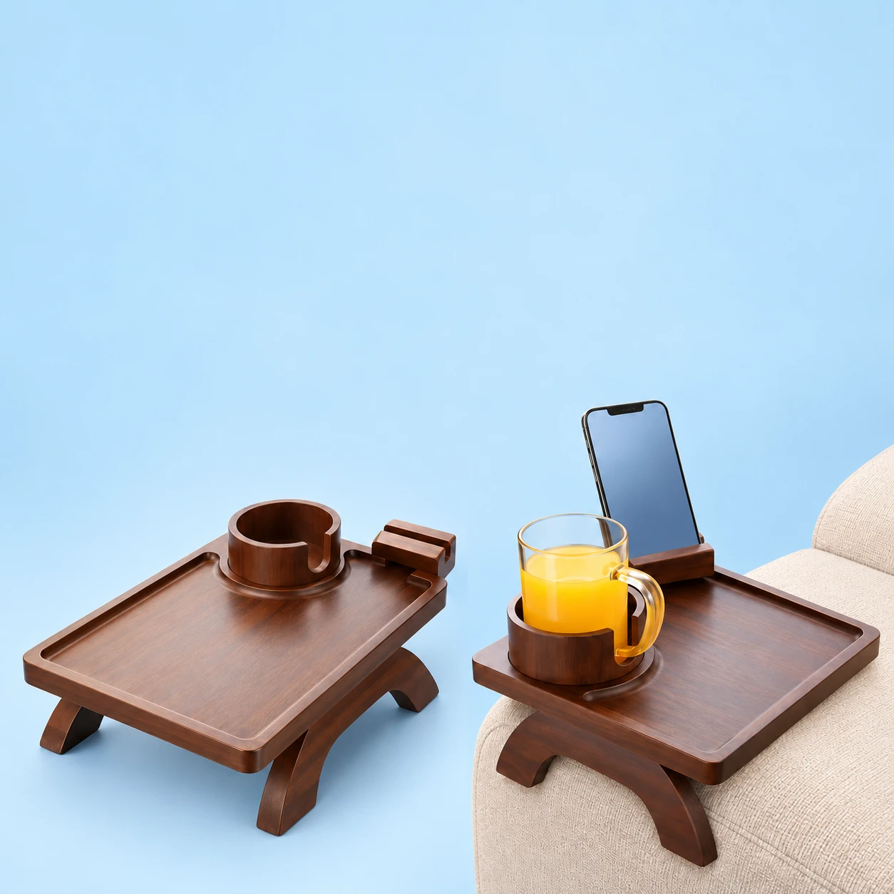 Complete brown sofa-arm tray at left, with its fixed notched cup sleeve, raised phone groove and two shaped lower supports; the same tray holds a demonstration phone and glass over a sofa arm at right on pale blue., square composition