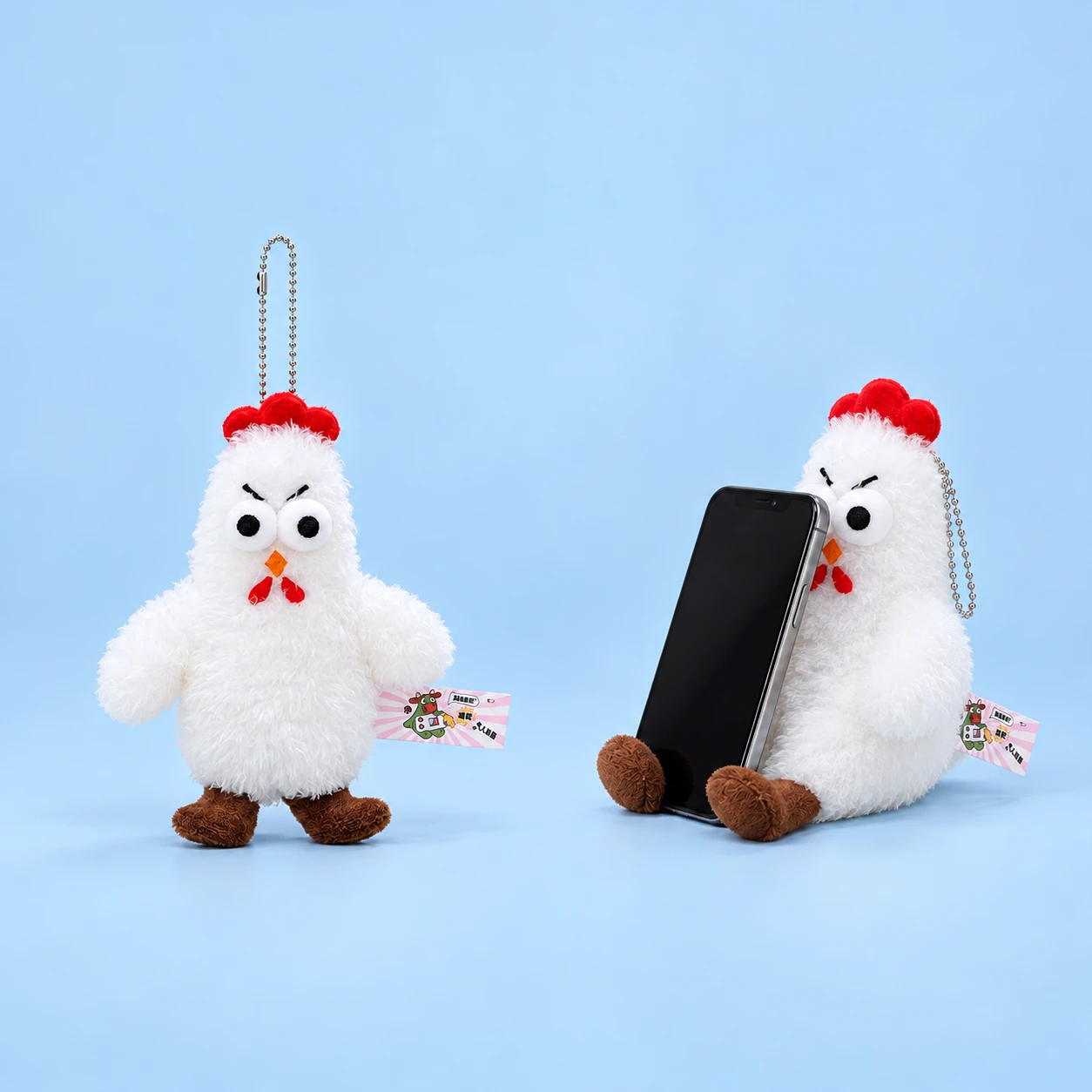 White red-comb chicken plush phone rest with decorative ball chain shown complete and supporting an illustrative phone, square composition