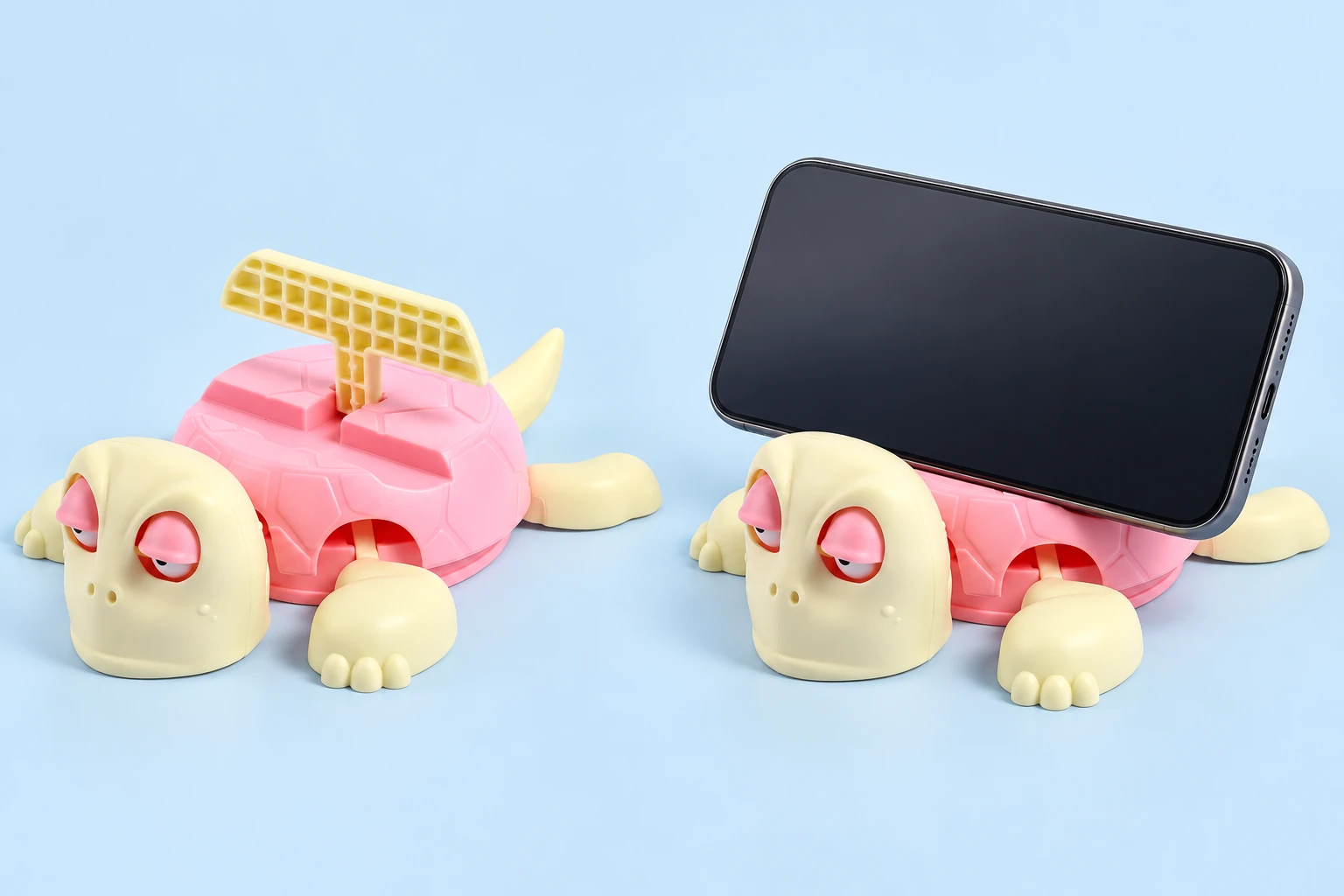 Pink-shell turtle phone stand with folding T-shaped backrest, shown alone and supporting a landscape phone