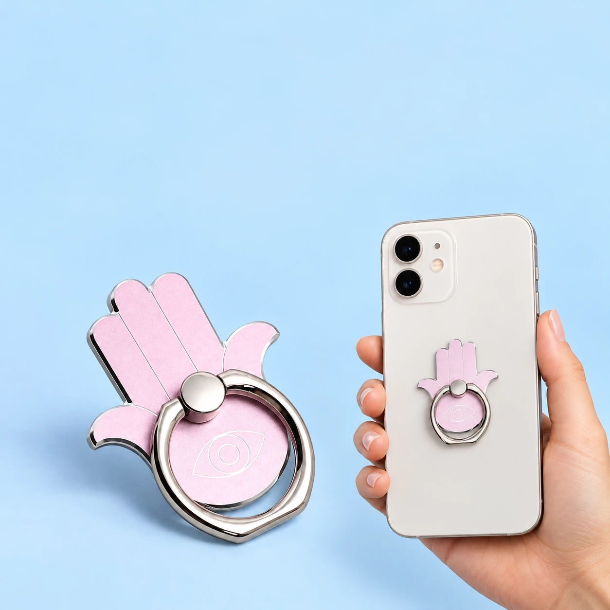 Pale-pink Hamsa hand phone ring with outlined palm eye, complete and closed on a hand-supported phone with hidden rear attachment, square composition