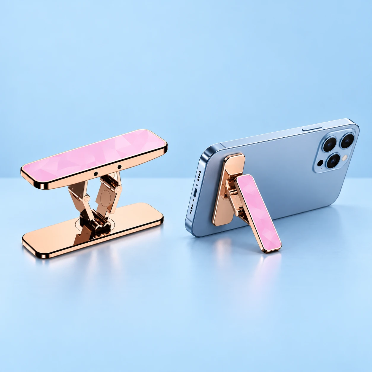 Complete pink and rose-gold-tone twin-link phone-back kickstand at left; the same kickstand supports a landscape demonstration phone with its original folding blade at right on a pale-blue background., square composition