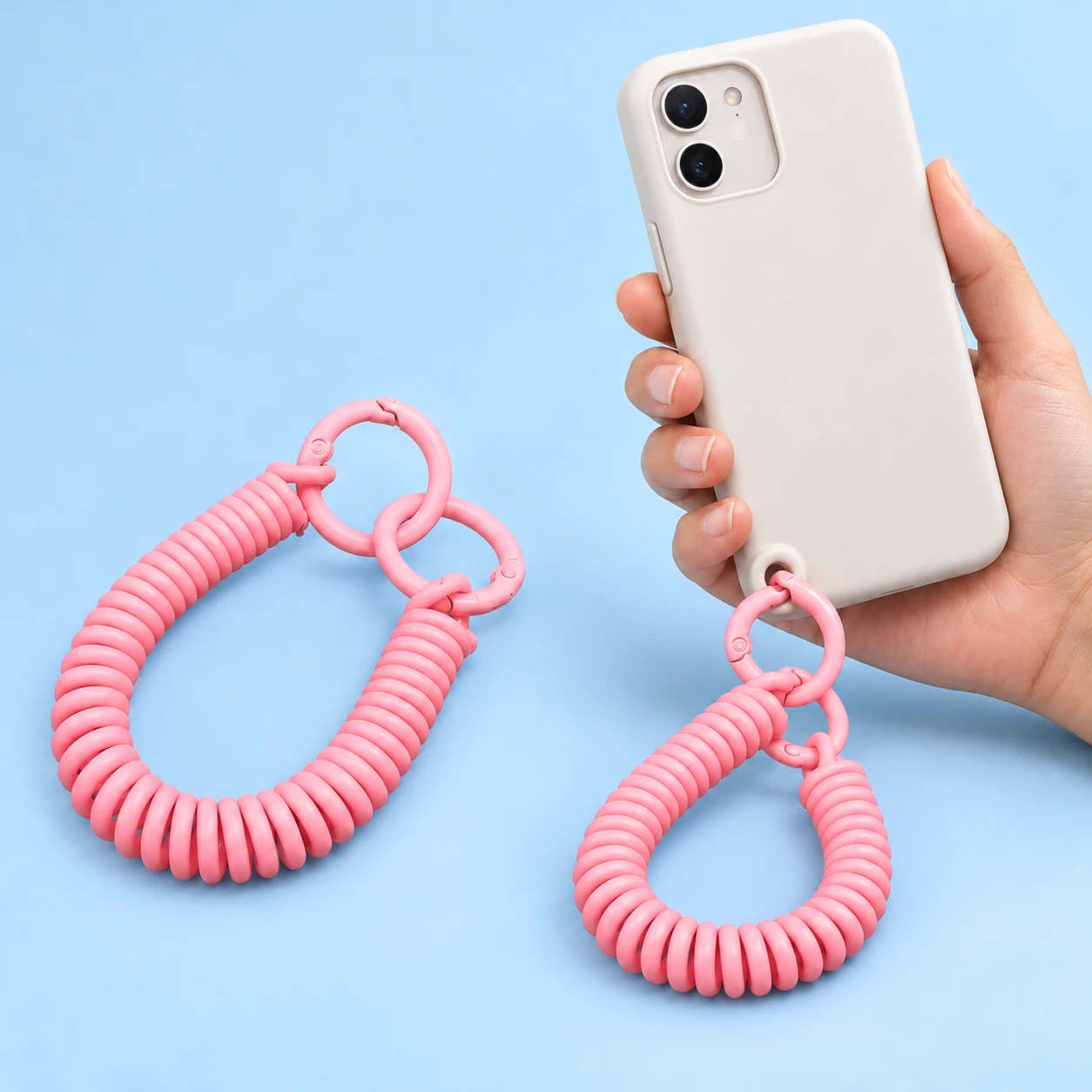Pink helical phone wrist tether with exactly two original round gates, shown complete and attached directly to a compatible case eyelet.