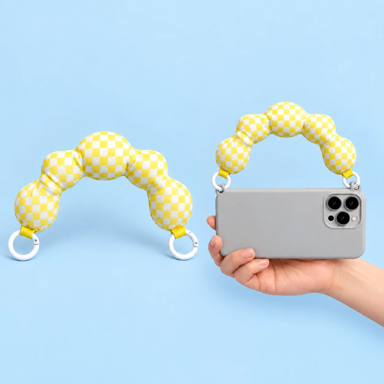 Yellow-and-white check five-lobed padded phone handle with two original white round gates, shown complete on the left and directly attached to two integral case eyelets on a hand-supported phone on the right. Phone and case not included., square composition