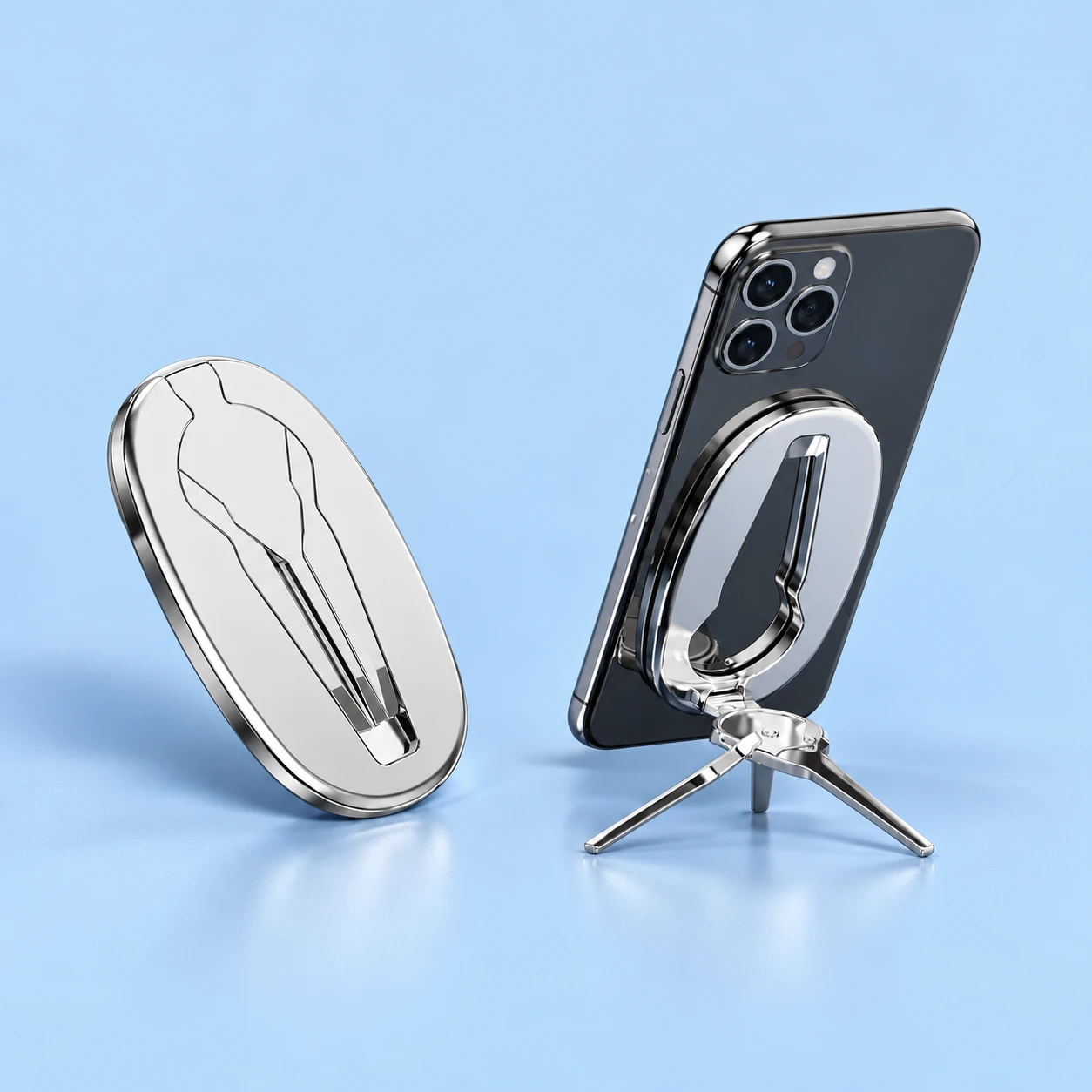 Complete folded silver oval magnetic phone-back stand at left; the same stand supports a portrait demonstration phone on its original split folding feet at right, against a pale-blue background., square composition