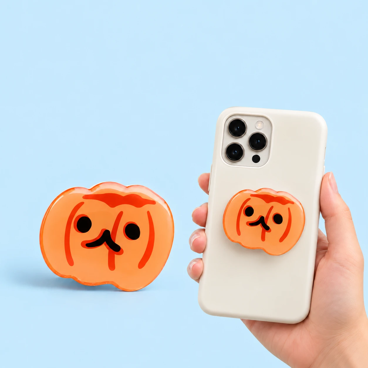 Orange pumpkin-face expandable phone grip with conservative closed phone-back placement, square composition