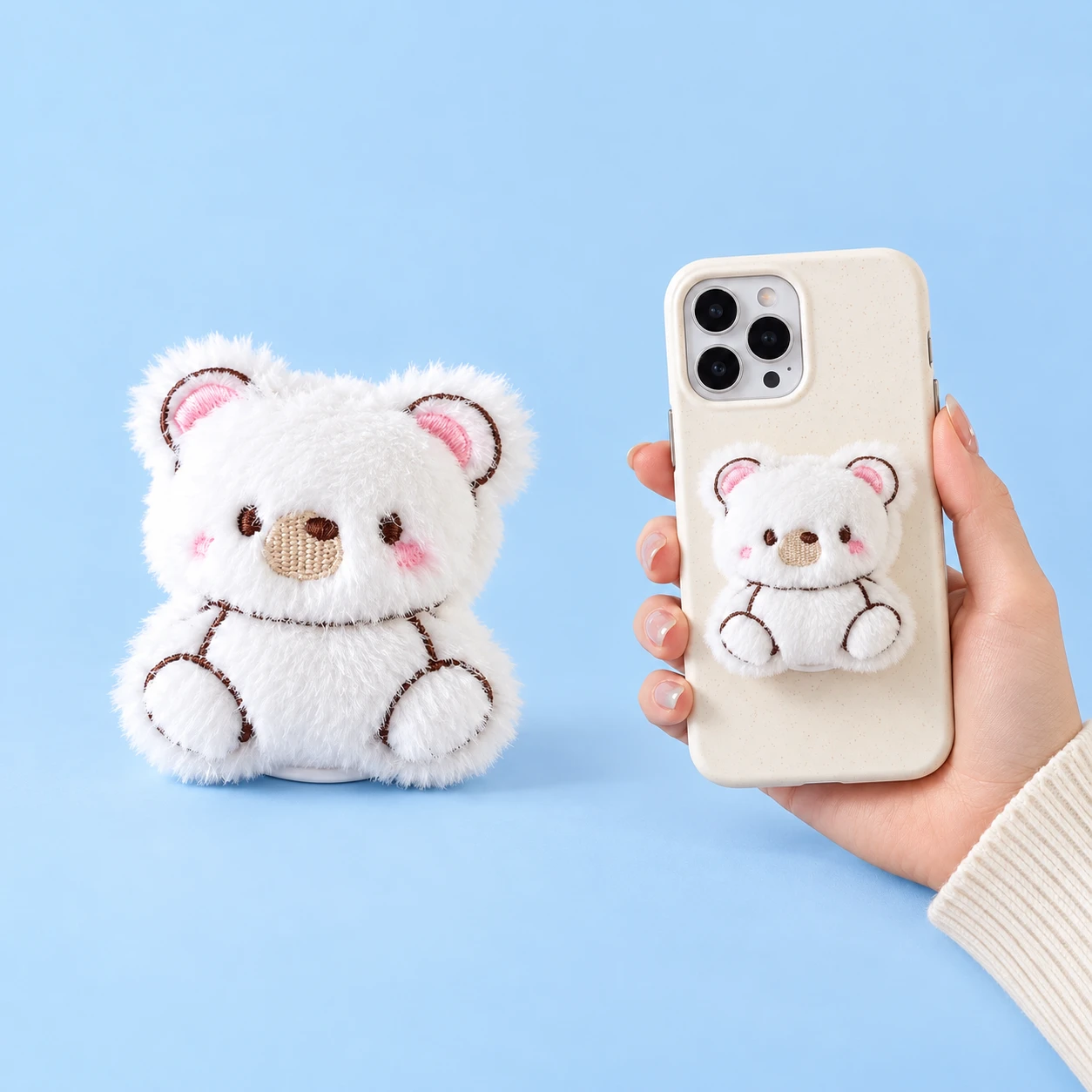 White embroidered seated bear plush phone grip shown complete and closed on a hand-held phone case, square composition