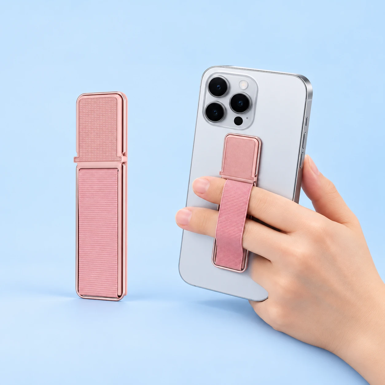 Rose-gold phone finger strap with original elastic band and stowed single wire kickstand left; the same holder attached to a hand-supported phone right on pale blue. Phone not included., square composition