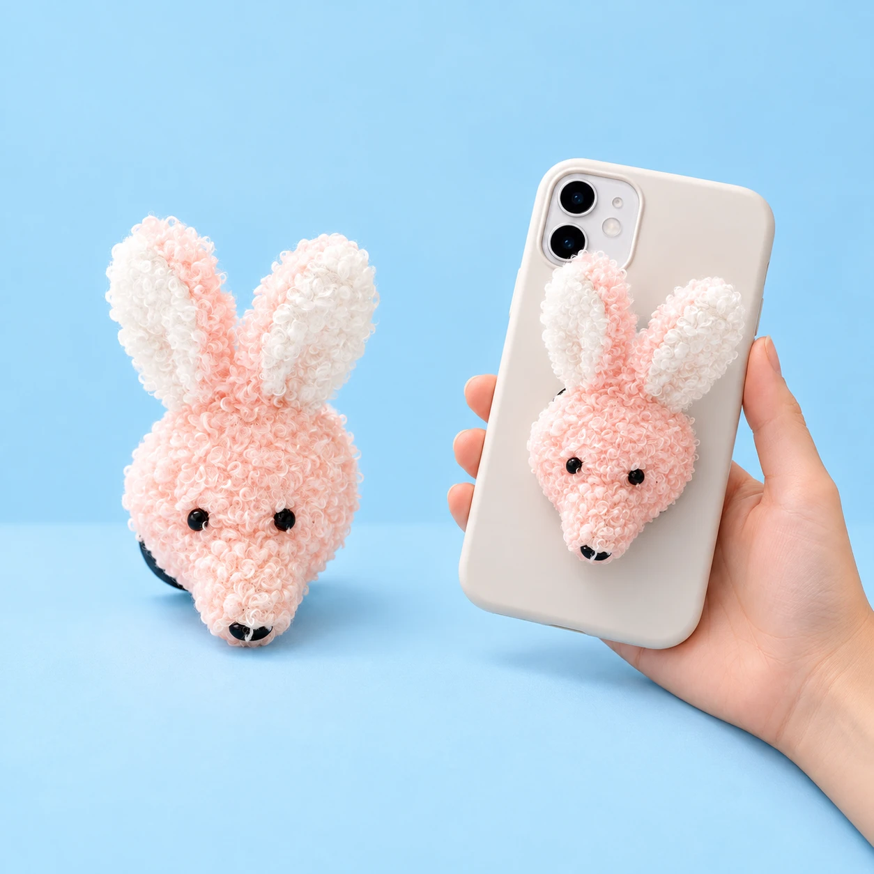 Pastel pink curly plush rabbit-head phone grip shown complete and closed on a hand-held phone case, square composition