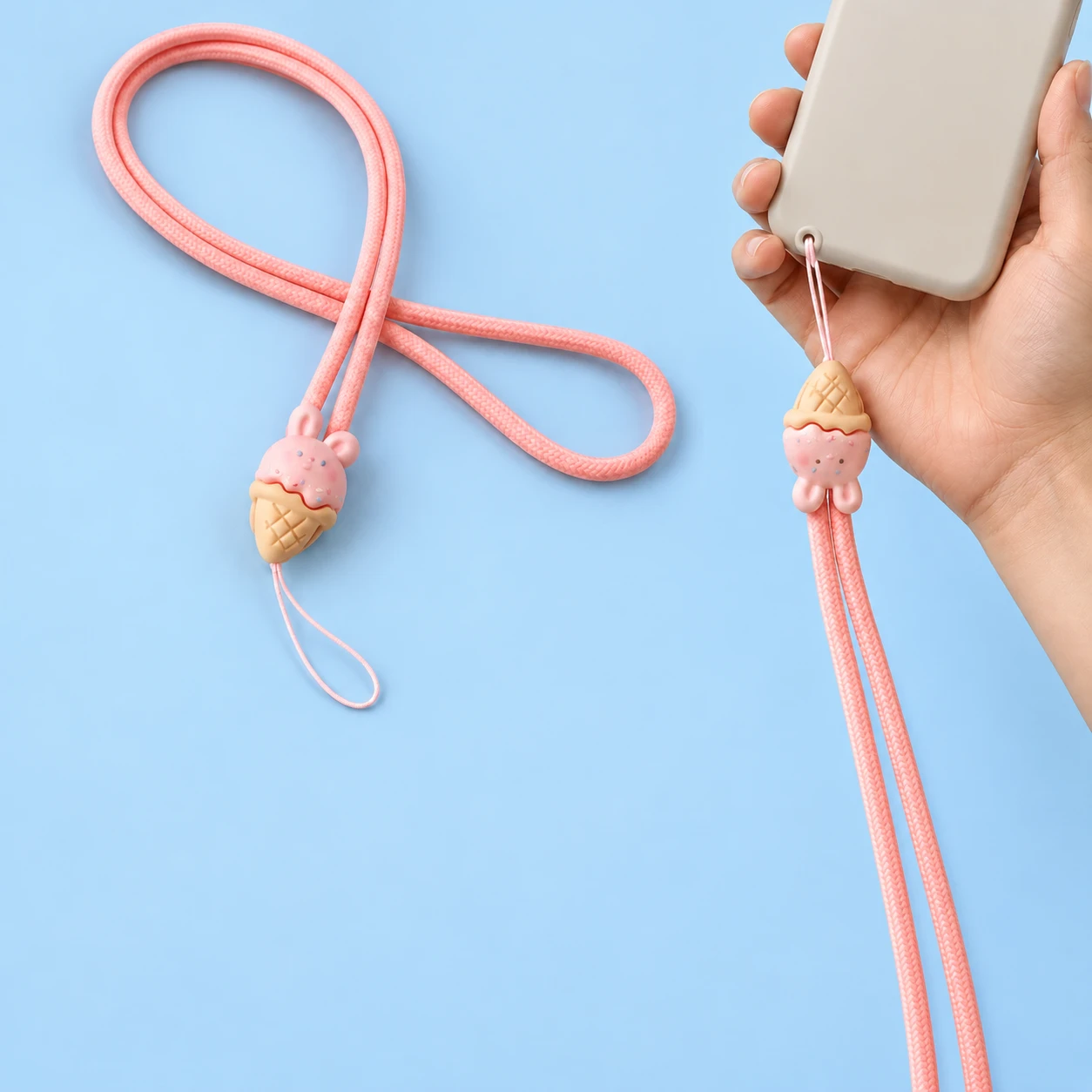 Pink long-cord lanyard with bunny ice-cream-cone charm and thin case-eyelet tether, shown complete and beside a hand-supported phone, square composition