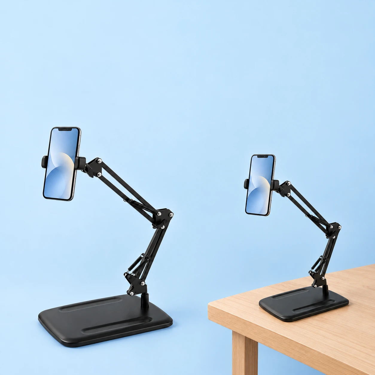 Black rectangular plate-base spring-arm phone stand on pale blue, shown complete with a demonstration phone at left and the same stand holding a demonstration phone on a desk at right. Both phones and the desk are not included., square composition