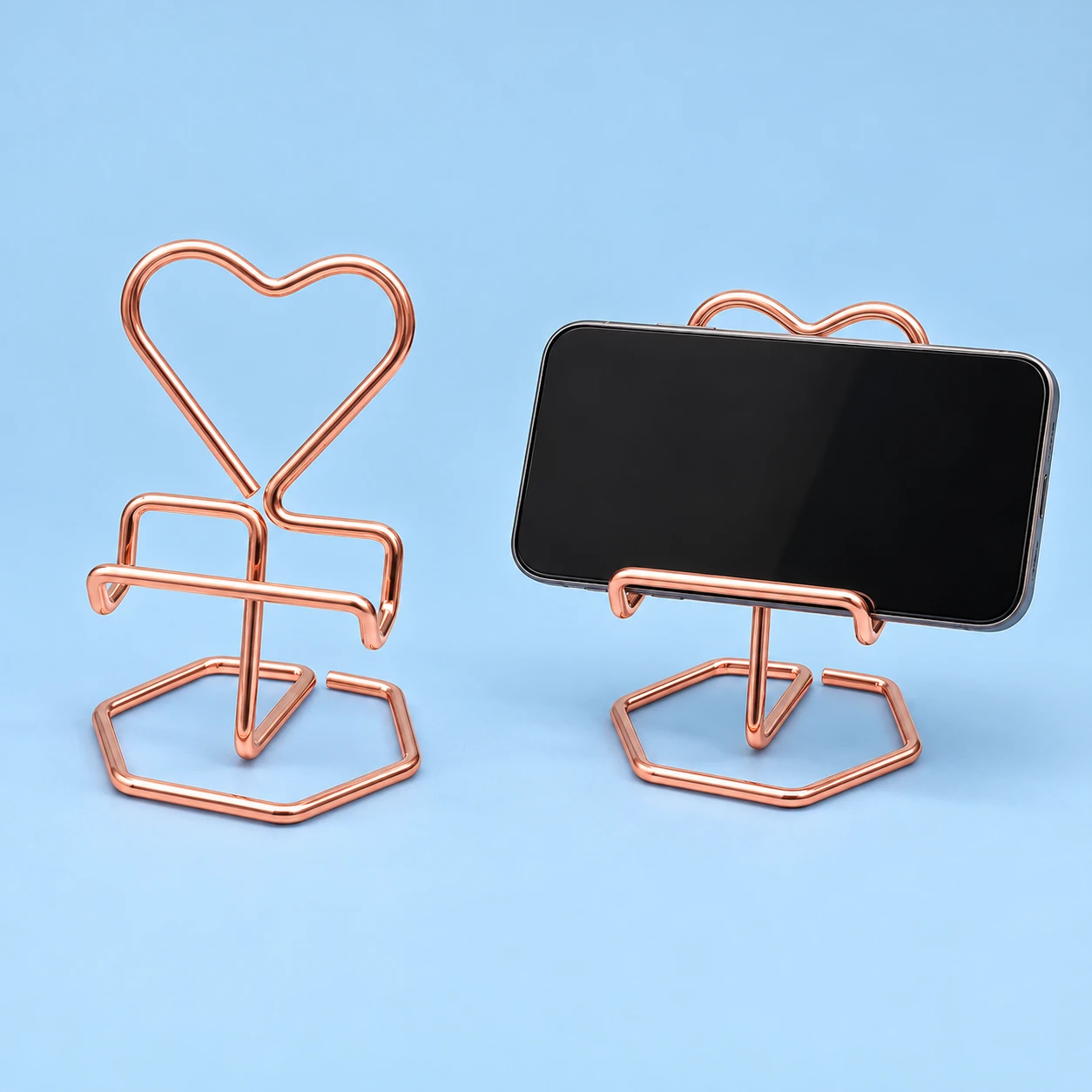 Rose-gold-colored hexagonal-base heart wire phone stand, isolated and supporting a landscape phone