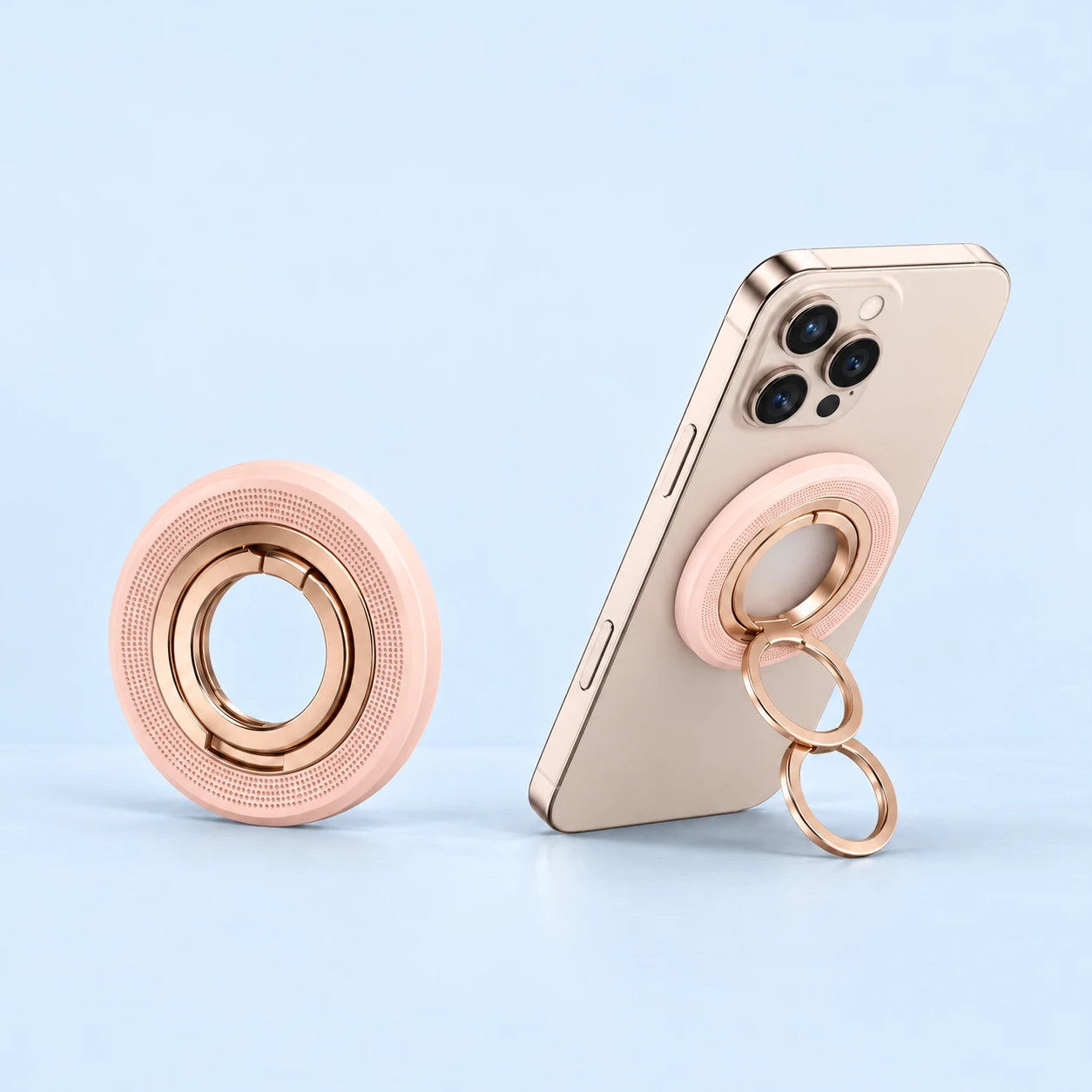 Pastel pink linked-ring magnetic phone stand shown folded and supporting a demonstration phone, square composition