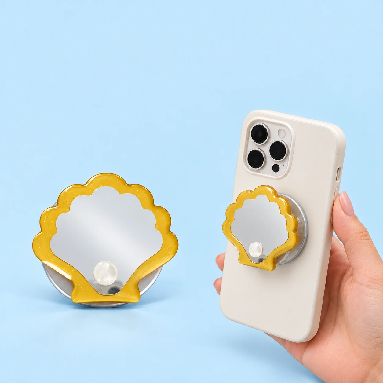 Yellow shell-mirror expandable phone grip with pearl-effect detail, shown alone and mounted on a held phone, square composition