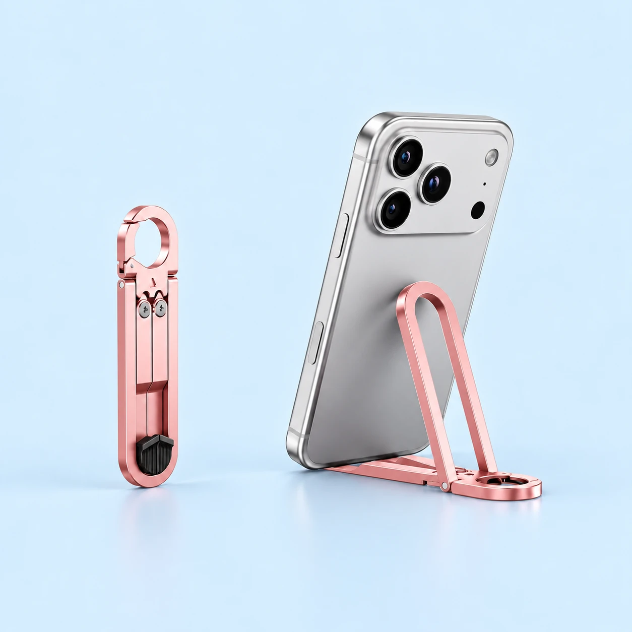 Pink oval-loop folding keychain phone stand shown folded and supporting a phone on its split rails, square composition