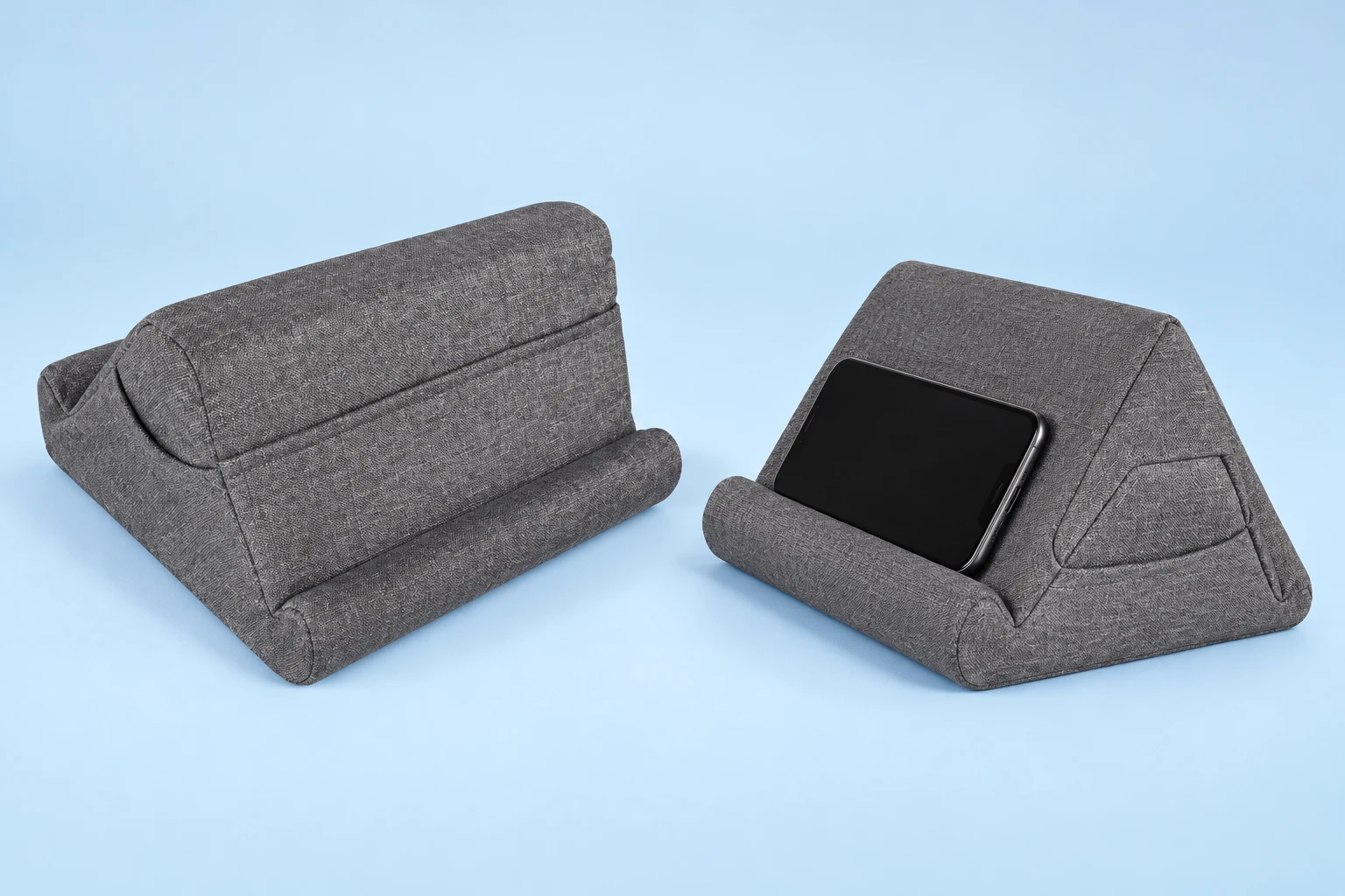 Complete medium-gray peaked foam reading cushion shown empty from the rear beside an intended landscape-phone illustration, with original opposed lower retaining rolls and side pocket on pale blue; phone not included.