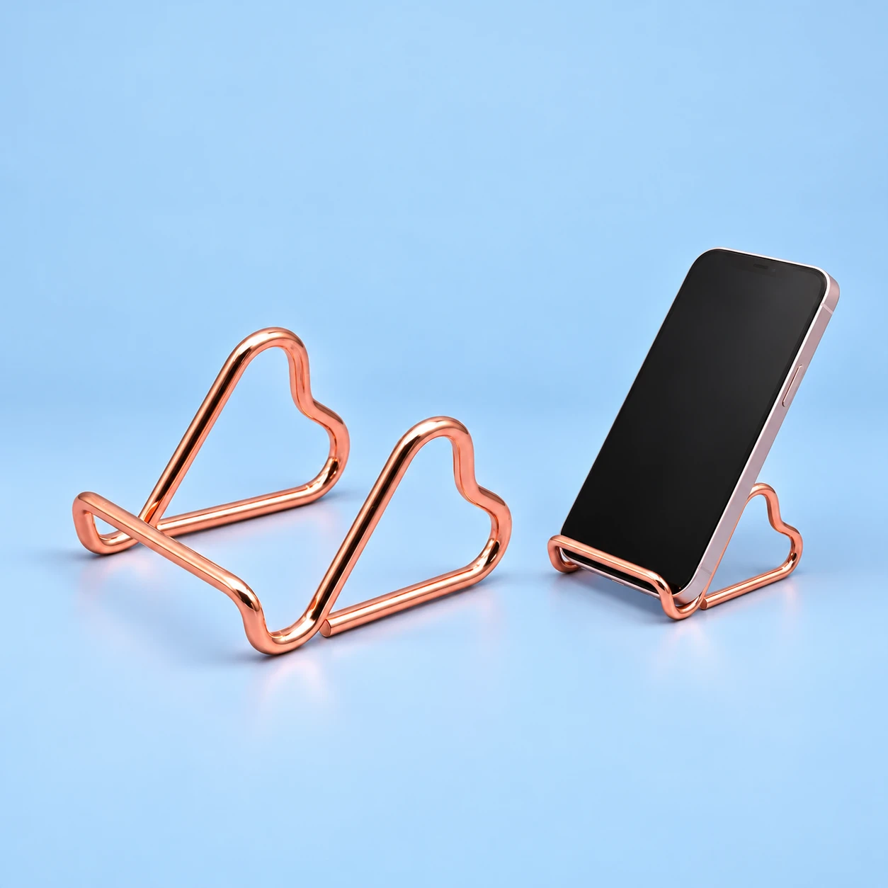 Rose-gold twin side-heart wire phone stand, isolated and supporting a portrait phone, square composition