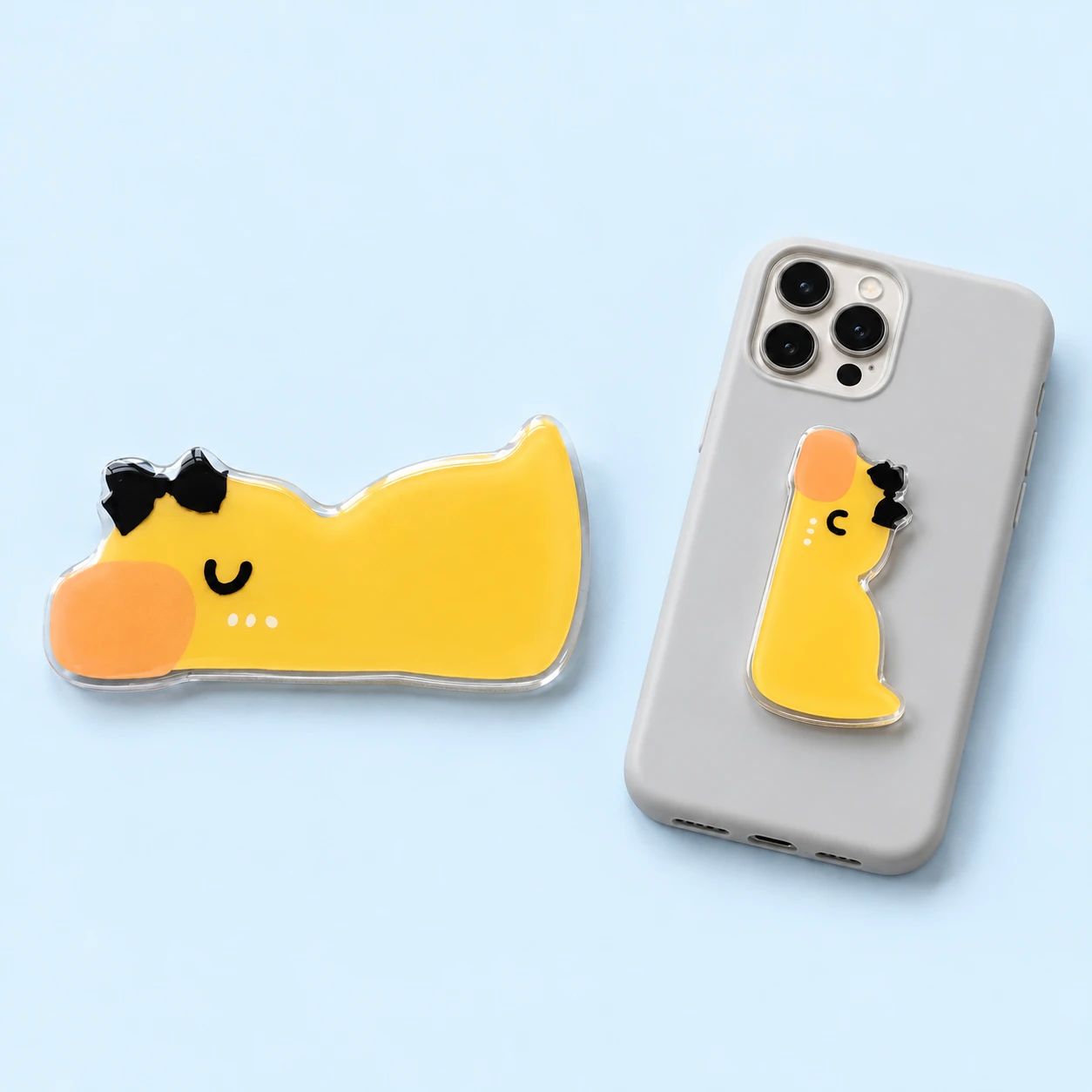 Yellow duck-shaped folding phone kickstand with black bow and closed phone-back placement, square composition