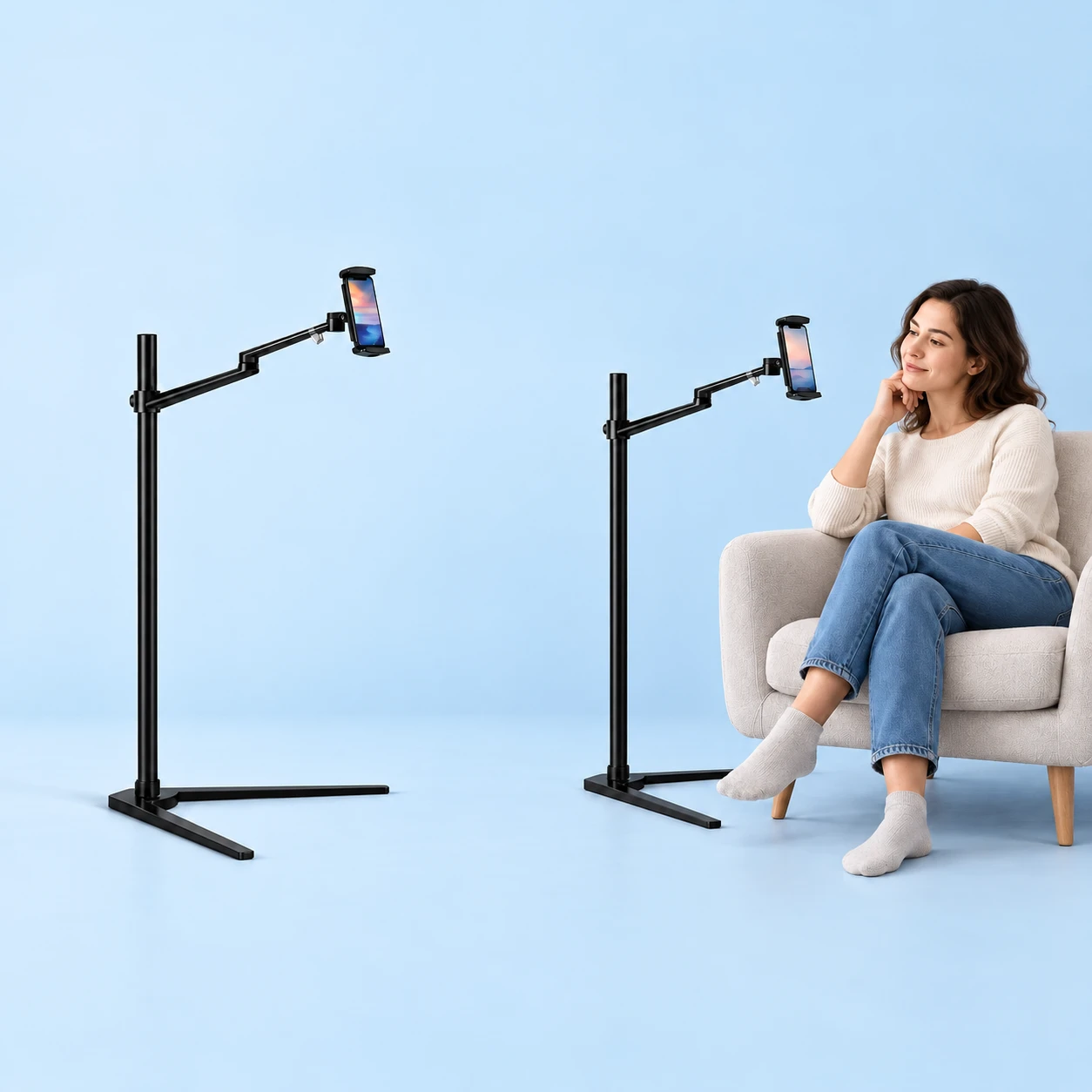 Complete black open-runner swing-arm floor phone stand with a demonstration phone on the left, and the same stand holding a demonstration phone beside a seated adult on the right, against a pale-blue background. Demonstration phones are not included., square composition