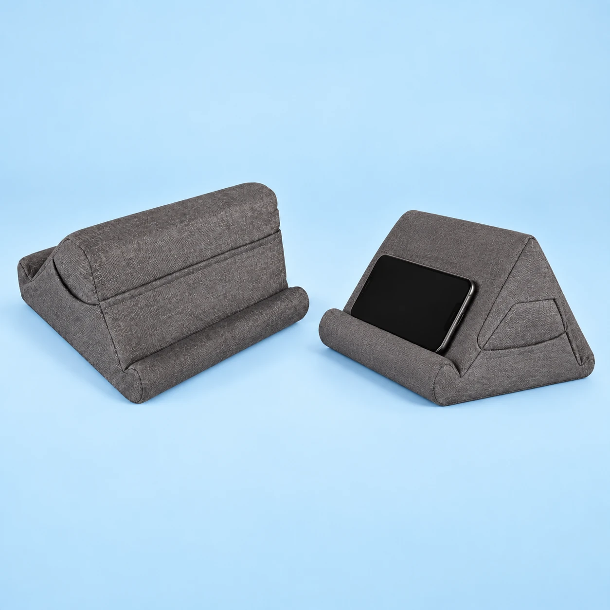 Complete medium-gray peaked foam reading cushion shown empty from the rear beside an intended landscape-phone illustration, with original opposed lower retaining rolls and side pocket on pale blue; phone not included., square composition