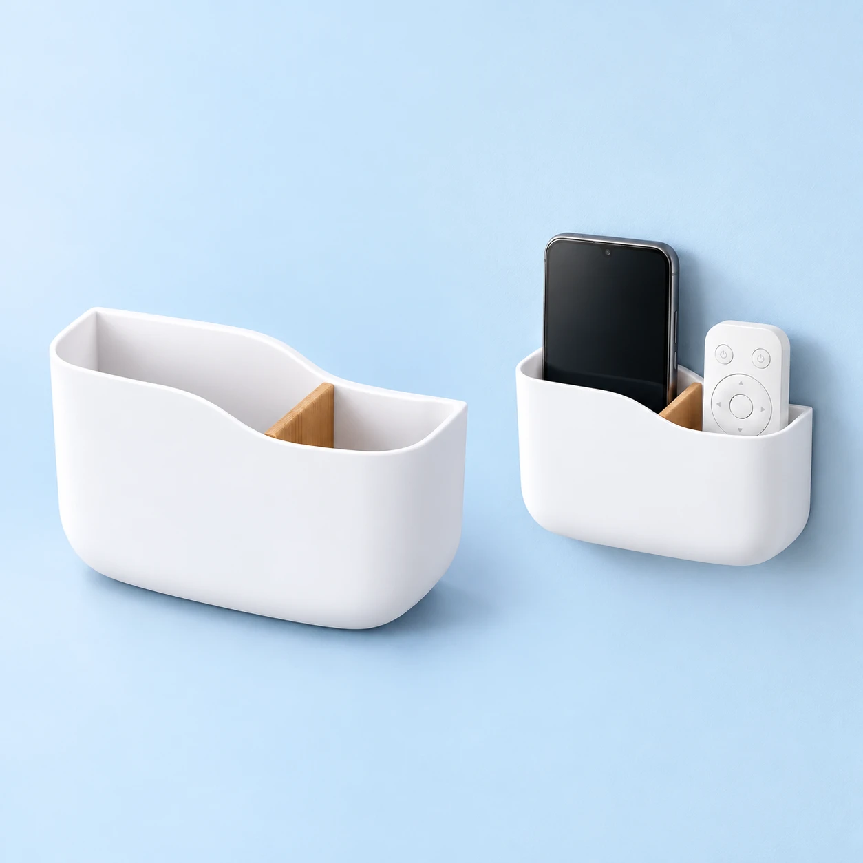 White divided wall phone pocket with removable wood-look divider, shown empty and mounted on a dry wall holding an illustrative portrait phone and remote, square composition