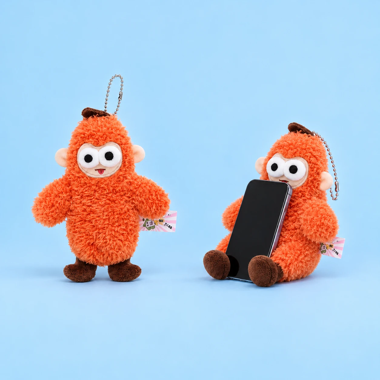 Orange round-eared monkey plush phone rest with decorative ball chain shown complete and supporting an illustrative phone, square composition