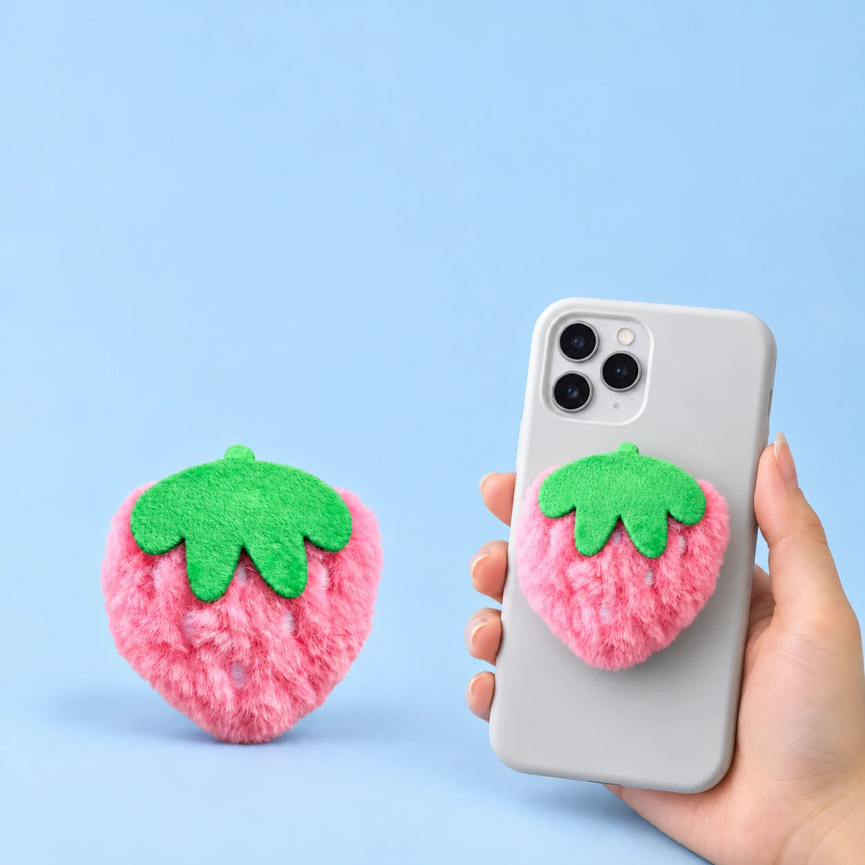 Pink plush strawberry phone grip and conservative closed phone-back placement, square composition