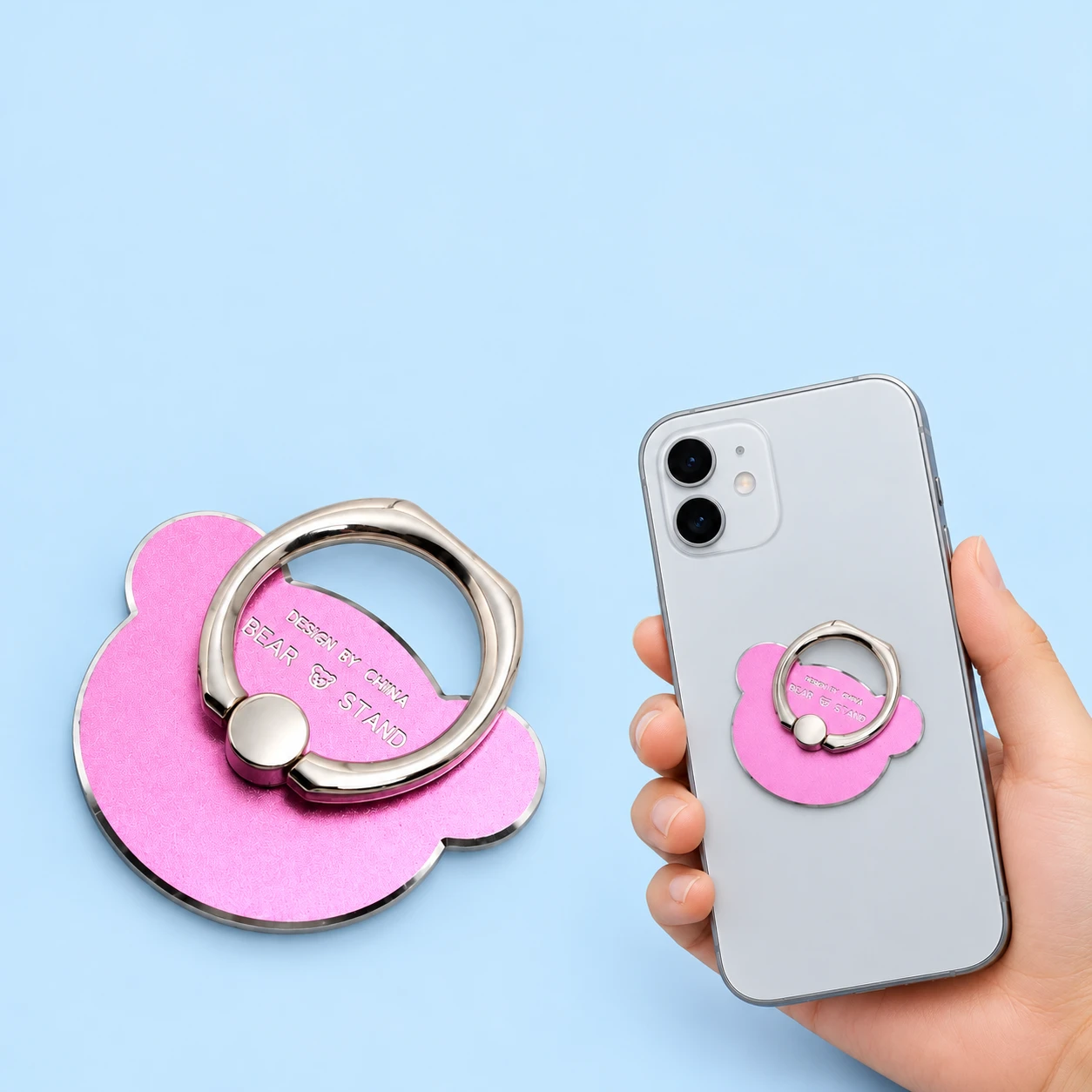 Pink metal bear-head phone ring with small round ears, shown complete and closed on a hand-supported phone with rear fixing hidden, square composition