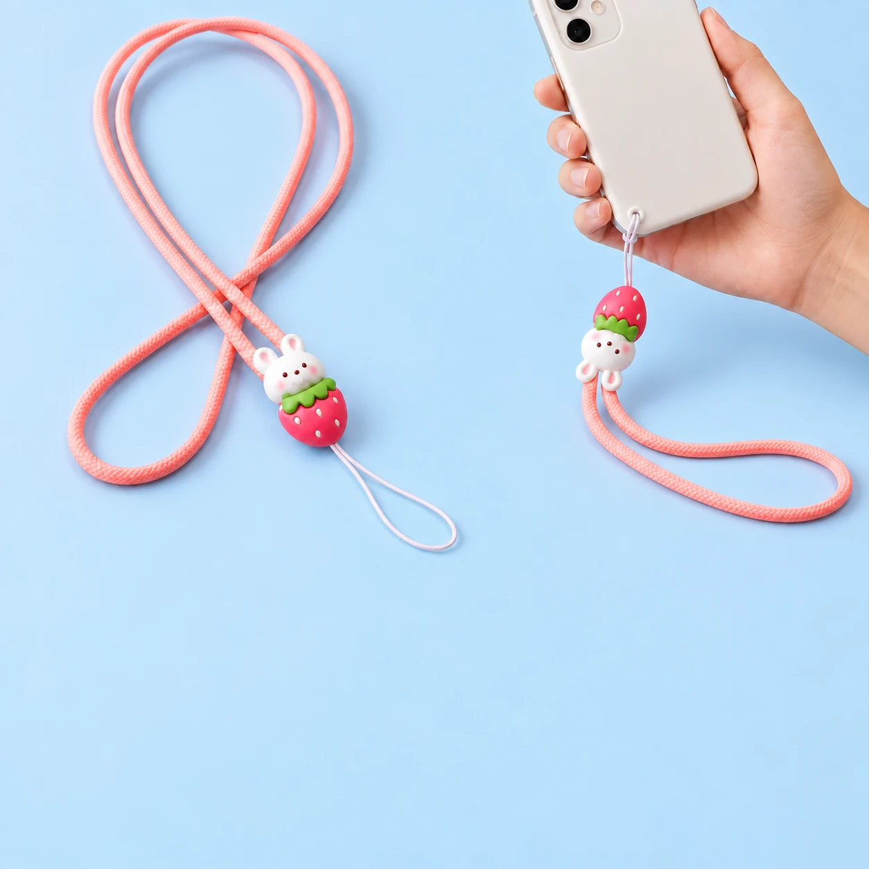 Pink strawberry bunny phone lanyard shown complete and connected by its thin string loop to a phone-case eyelet, square composition
