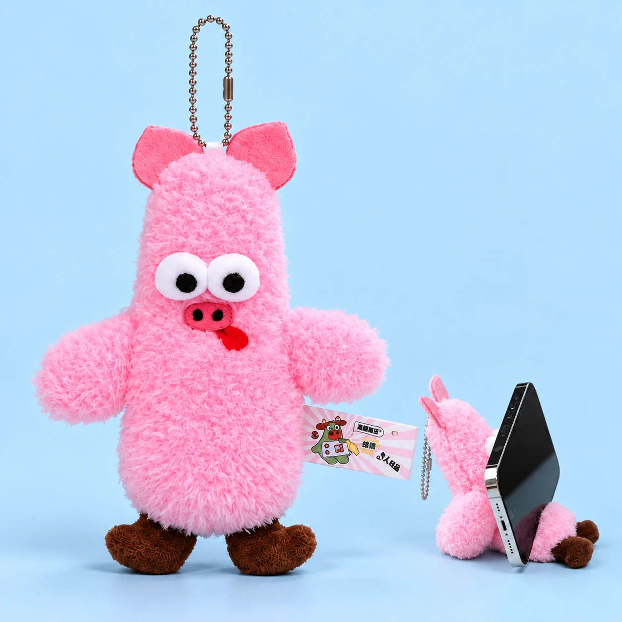 Pink googly-eyed pig plush phone rest, shown complete and seated with a phone resting against its torso