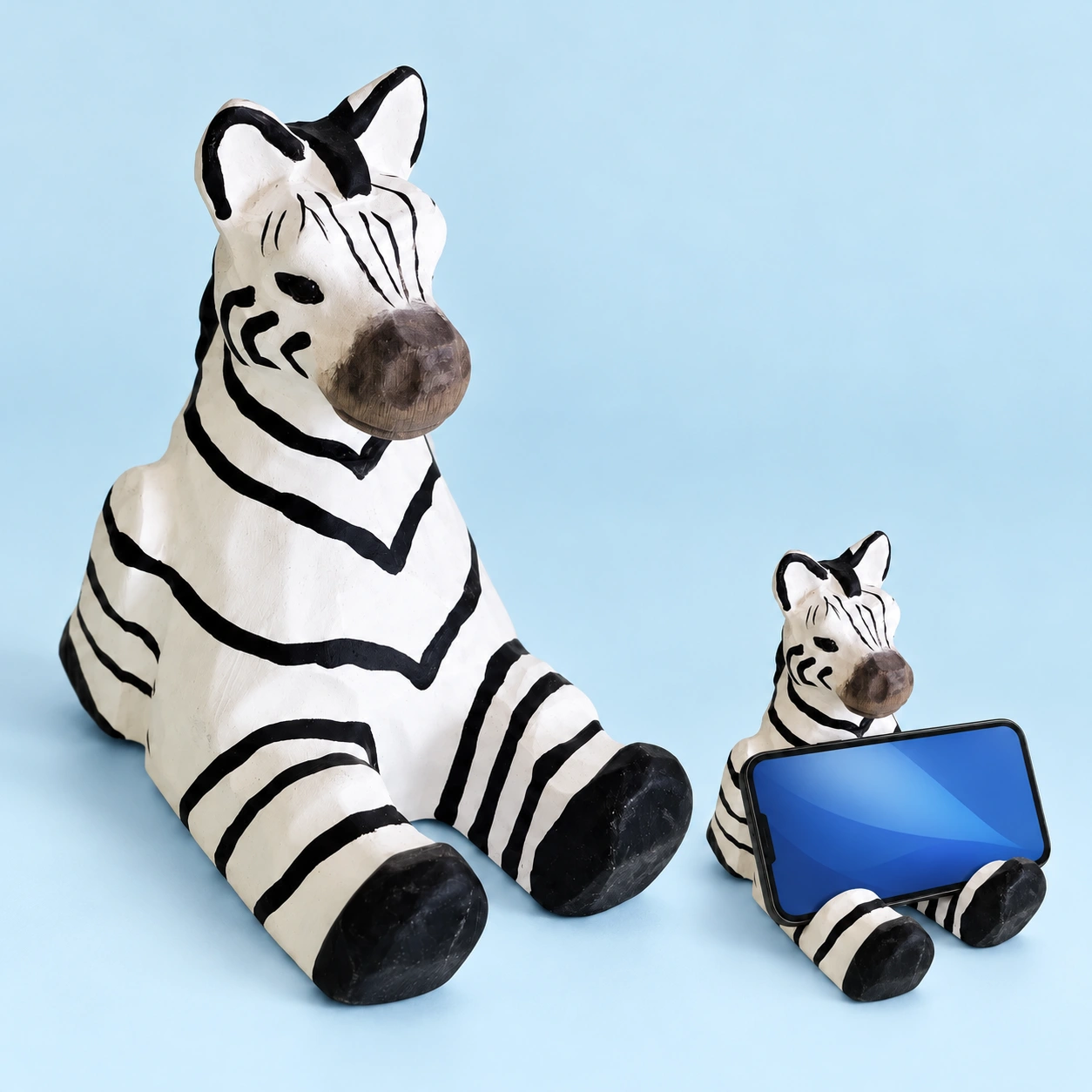 Wooden zebra phone stand, complete striped stand left and landscape phone cradled behind raised hooves right; phone not included