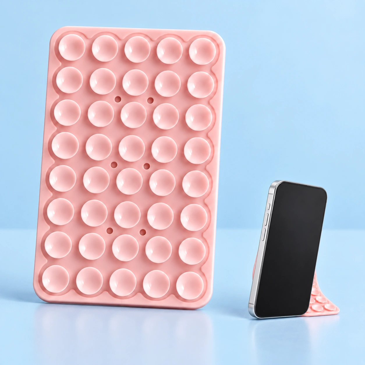 Pastel pink bendable suction phone stand, isolated and shown supporting a phone